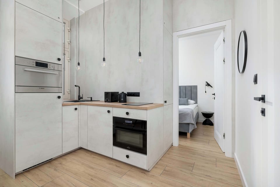 An ergonomic kitchenette in white and gray tones, equipped with modern built-in appliances and minimalist ceiling lighting.