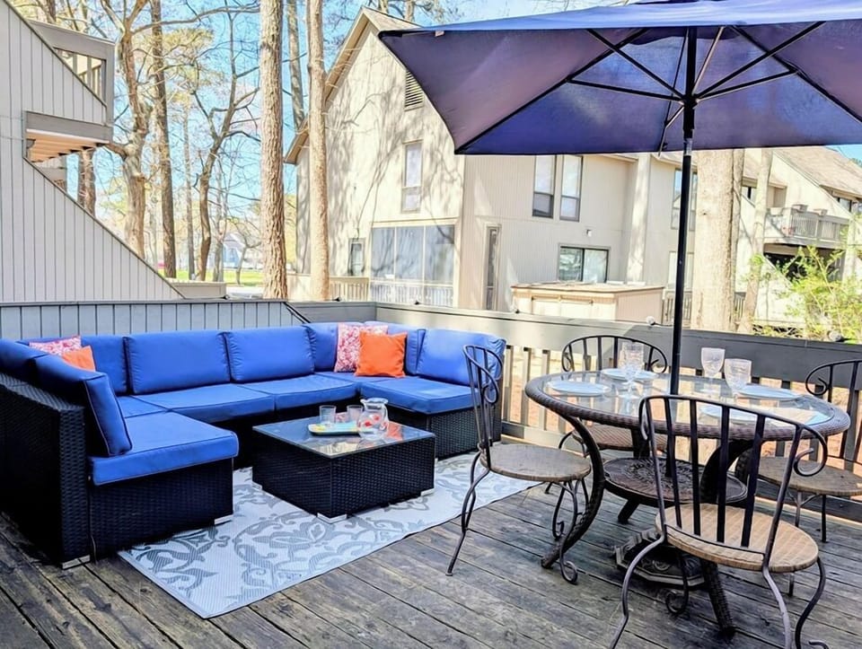 2306 Round Robin Way Sea Colony West Outdoor Deck Patio with Sec - A wooden outdoor deck patio space arranged with a blue cushion sectional sofa, a coffee table, and an umbrella-shaded dining table set.