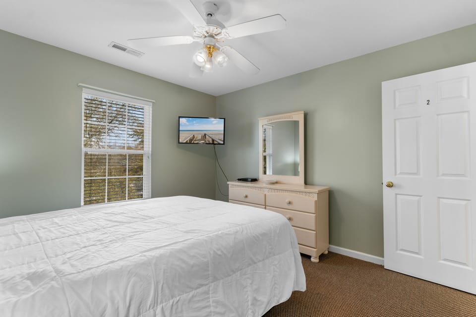 Rest peacefully in your serene bedroom with soft sage walls, ceiling fan, and TV for evening entertainment.