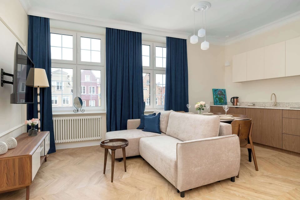 A spacious living and dining area shows the connection between the seating zone and the eating area. A modern chandelier hangs above the table, and navy blue curtains frame the large windows.