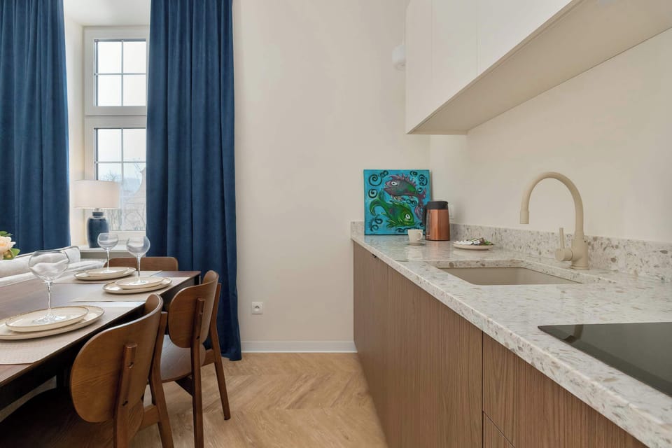 A minimalist kitchenette workspace features a white speckled countertop and a built-in cooktop. The lack of handles on the wood-toned cabinetry creates a smooth, contemporary look.