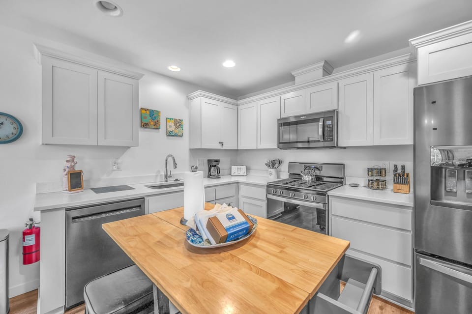 Your fully equipped kitchen invites culinary adventures with white cabinetry, stainless steel appliances, and a warm wood island for meal prep.