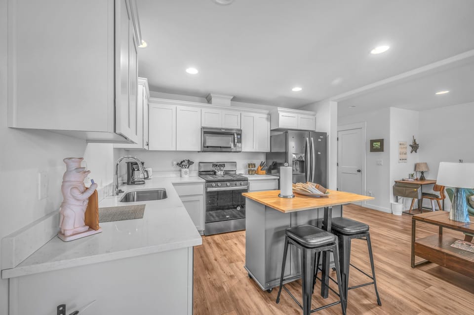 Your modern kitchen features sleek white cabinets, stainless steel appliances, and a convenient breakfast bar where you can enjoy morning coffee.