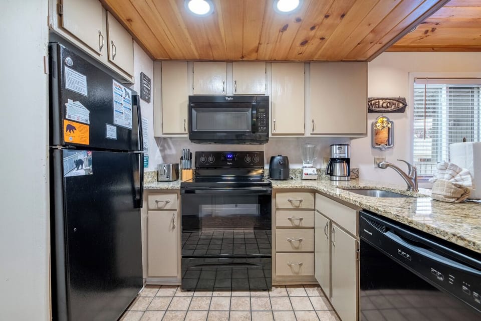 Cook your favorite meals in this well-equipped kitchen featuring granite countertops, full appliances, and warm wood ceiling details.