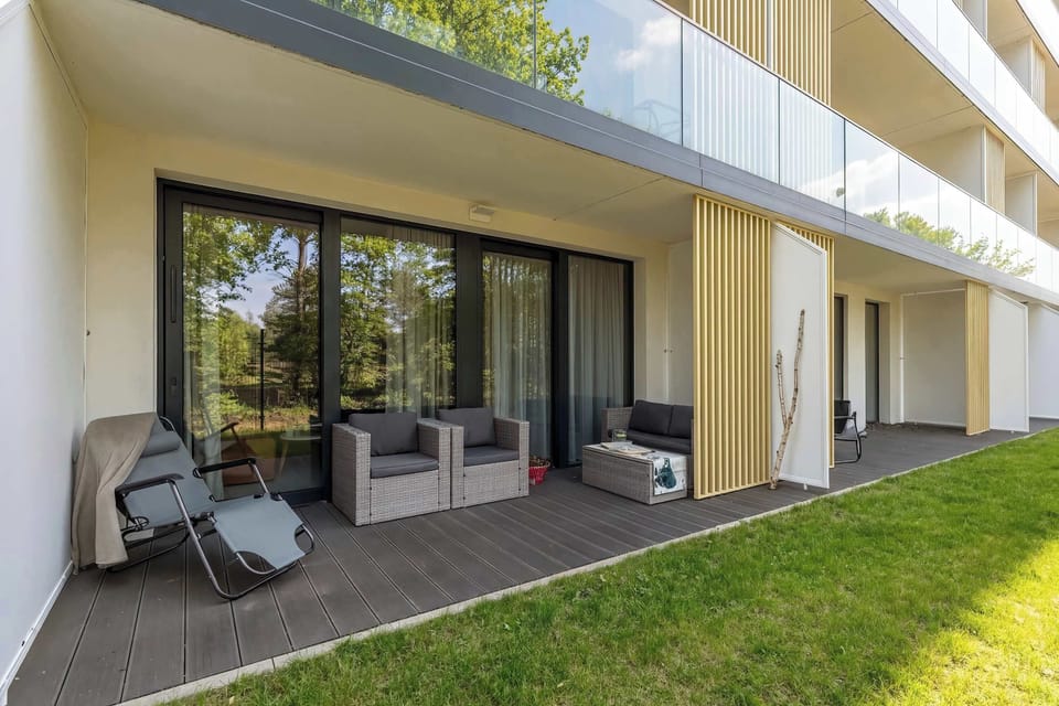 A ground-level patio with outdoor seating positioned next to a grassy area and building facade.