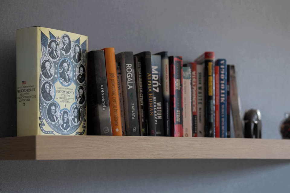 Wooden wall shelf is packed with a diverse collection of books, adding a personal and intellectual touch to the decor. The dark spines contrast beautifully against the muted grey wall behind them.