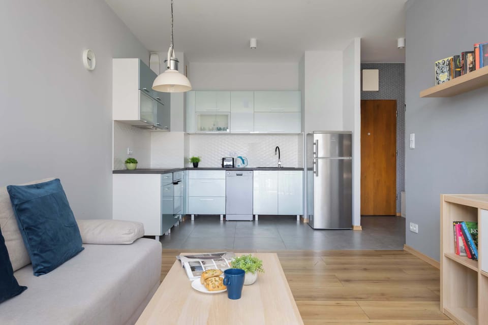 Brightly lit interior captures the transition from the soft seating area to the functional kitchen zone. Sunlight streams in from the side, highlighting the smooth textures of the floor and cabinetry.