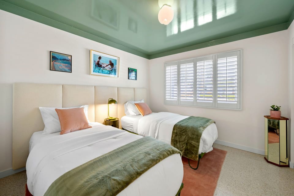 Your twin bedroom features fresh white linens, vibrant art, and natural light streaming through plantation shutters.