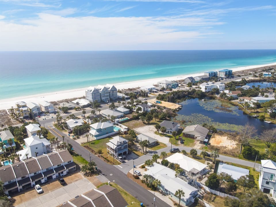 Aerial view of coastal community featuring pristine white sand beaches, turquoise waters, residential properties, and scenic lake areas.