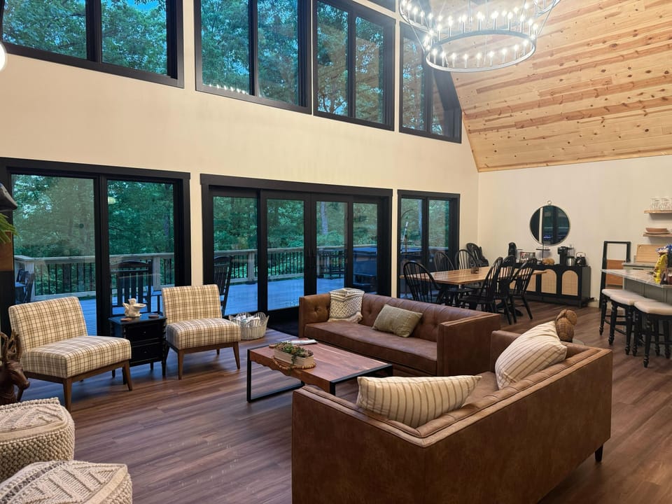 Living area with leather sofas, plaid armchairs, wood coffee table, and floor-to-ceiling windows overlooking the deck.