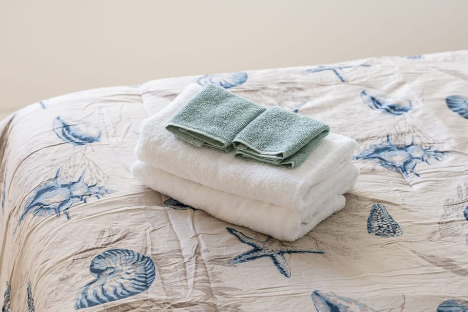 Fresh towels await on your cozy bed, perfectly prepared for your seaside getaway.