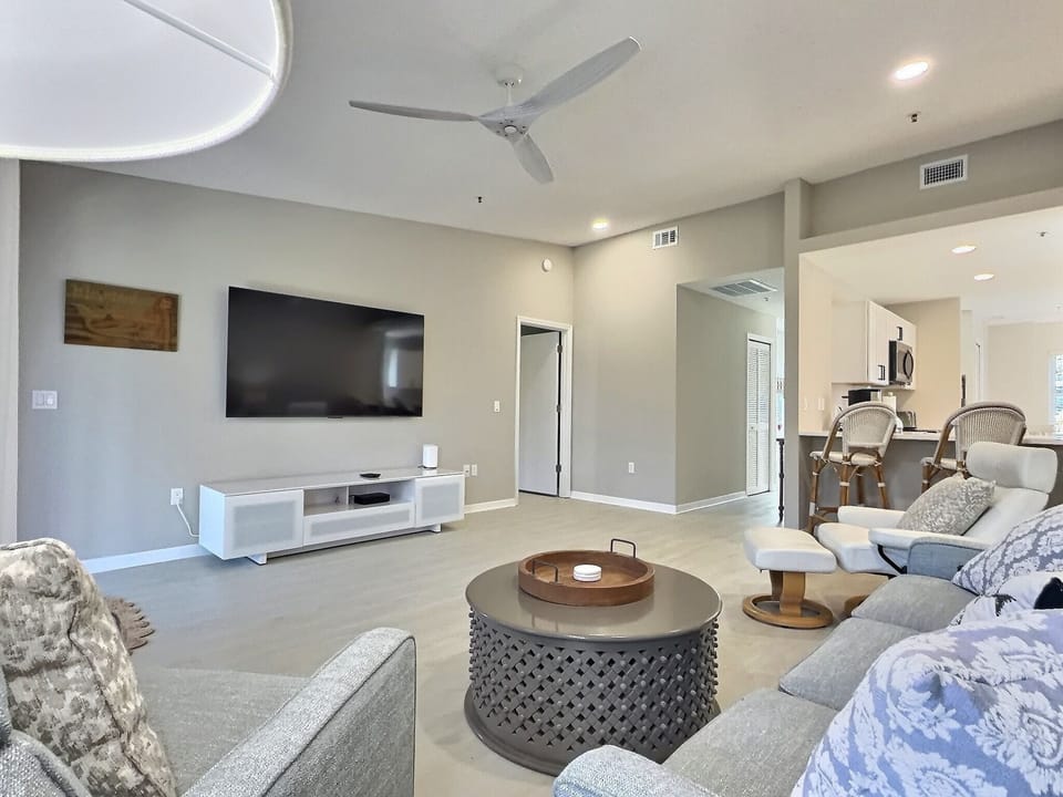 Open-concept living room with sectional sofa, wall-mounted TV, and direct access to the screened lanai