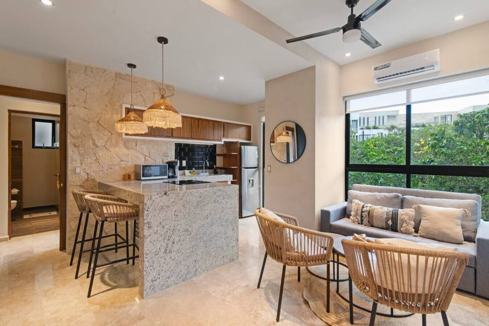 Bright and modern open-concept living space featuring a fully equipped kitchen, elegant stone finishes, and stylish seating—perfect for relaxing or entertaining.