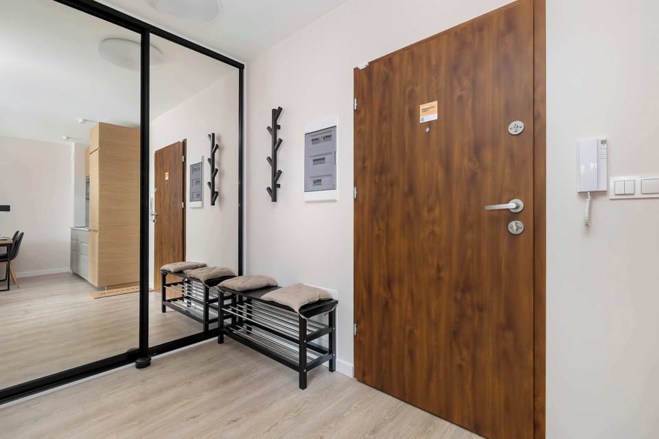 An entryway with a large mirror that makes the space appear larger, as well as a practical coat rack and bench by the front door.