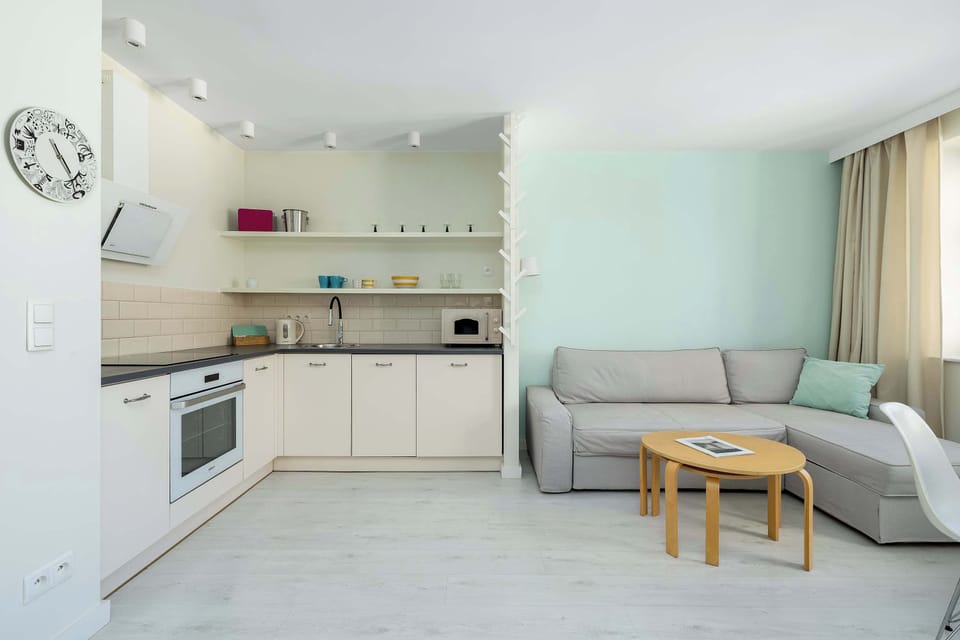 A compact kitchen corner with white cabinetry and open shelving. A small table and stool add functionality while keeping the space minimal and tidy.