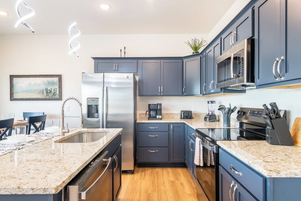 Your fully equipped kitchen features sleek blue cabinetry, granite countertops, and stainless steel appliances for effortless meal preparation.