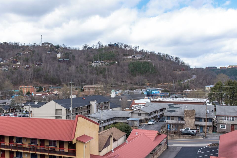 A charming hillside town spreads across rolling terrain, with residential buildings dotting the landscape under a partly cloudy sky.