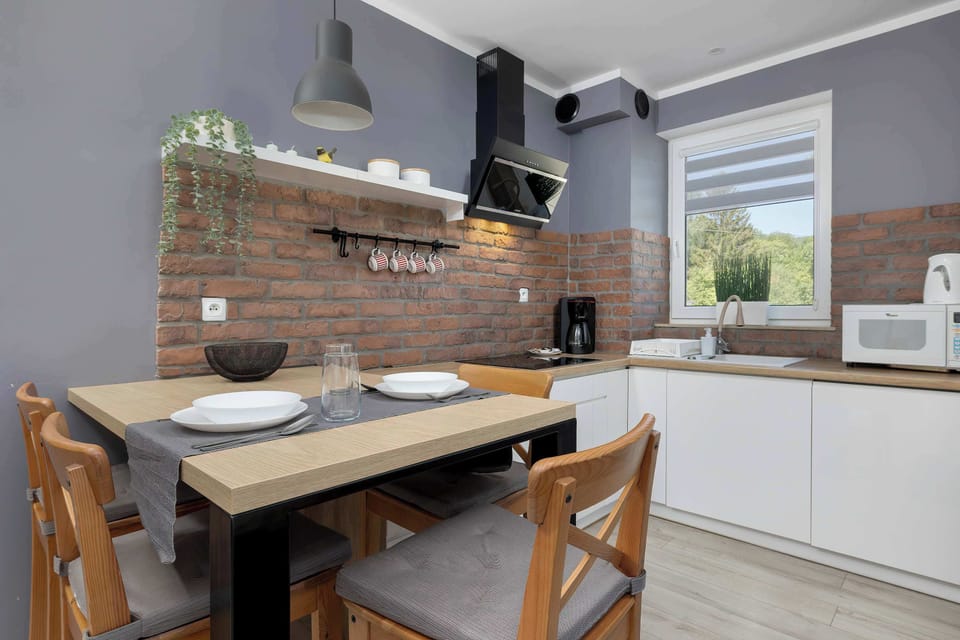A view of the kitchenette and dining area, showing a wooden table set for a meal. The cozy atmosphere of the interior is created by gray walls and black metal pendant lights hanging above the table.