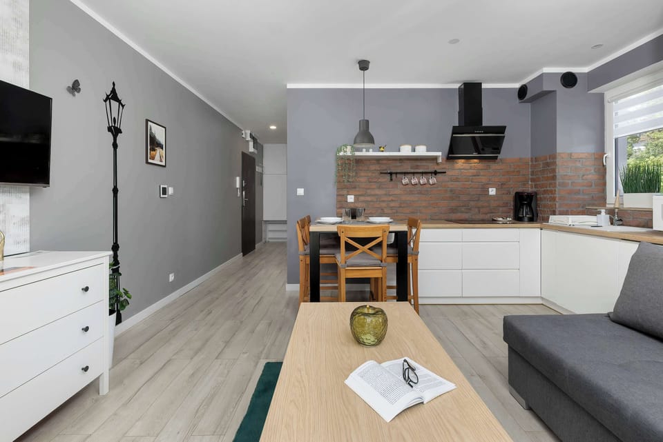 A view across the living room toward the kitchen, showing the apartment’s open floor plan with clearly defined zones. On the left is a white dresser, and on the right, a section of a gray sofa and a coffee table.