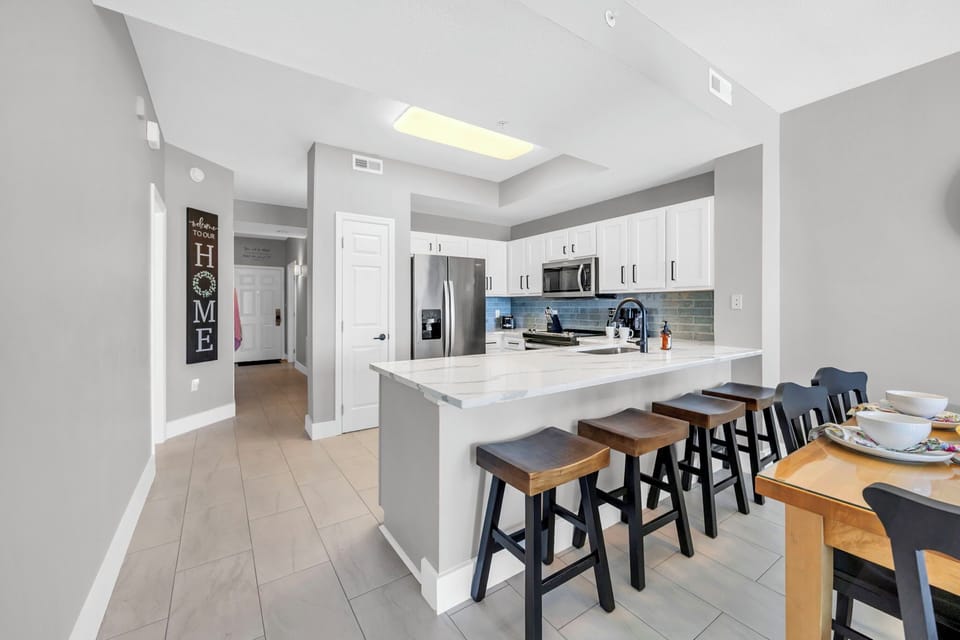 Your spacious kitchen features a large island with seating, stainless steel appliances, and modern white cabinetry ideal for cooking together.