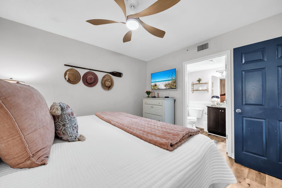 Step into your serene retreat with soft bedding, a gentle ceiling fan, and coastal-inspired decor. Through the doorway, your private ensuite awaits for your comfort.