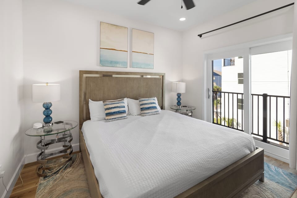 Step into your serene bedroom retreat with a plush bed and coastal-inspired accents. Natural light streams through the balcony doors, while the ceiling fan keeps you comfortable after a day of adventure.