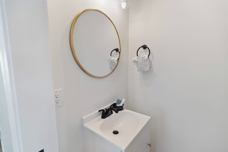 Freshen up in your modern bathroom featuring a gleaming white vanity and elegant gold-framed mirror. The sleek fixtures and crisp design create a bright, welcoming space for your morning routine.