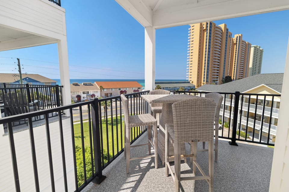 A covered balcony frames a partial ocean view alongside nearby high-rises, offering a peaceful outdoor retreat with comfortable seating and coastal breezes.