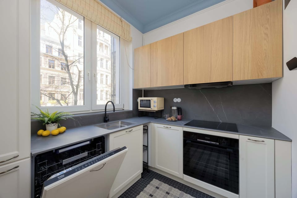 An L-shaped kitchen featuring modern wood-grain and white cabinetry, a built-in oven, dishwasher, induction cooktop, and a window with a view.