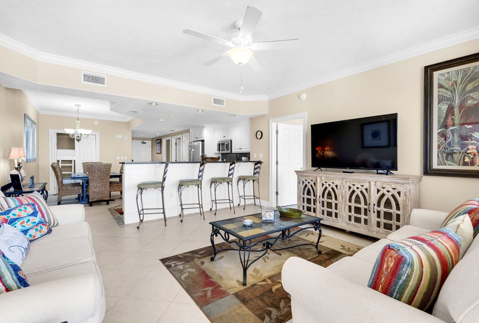 Relax in your spacious open-concept haven with plush seating, tropical artwork, and modern kitchen perfect for gathering.