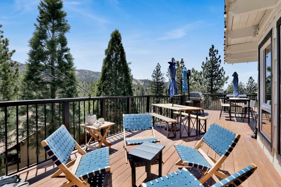 Outdoor deck with a jacuzzi, BBQ grill, dining table, and comfortable seating, offering beautiful mountain and pine tree views in a peaceful setting.