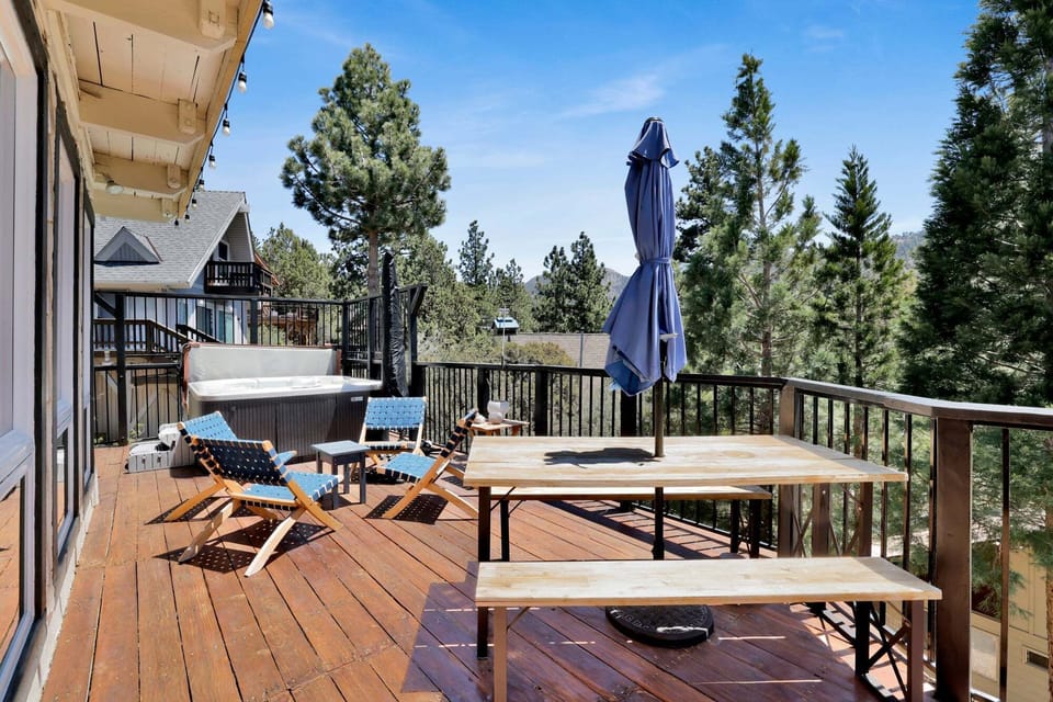 Outdoor deck with a jacuzzi, BBQ grill, dining table, and comfortable seating, offering beautiful mountain and pine tree views in a peaceful setting.