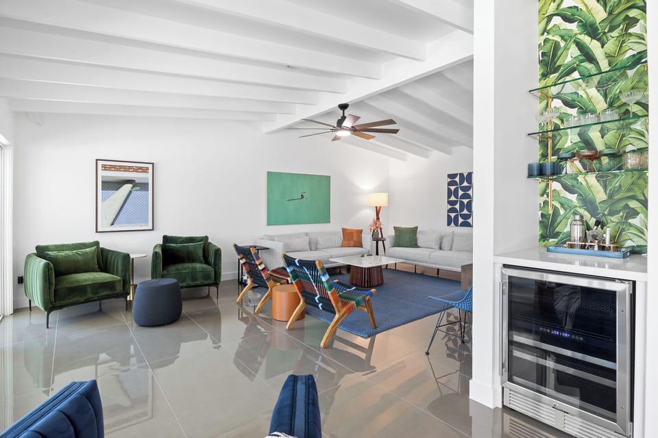 Relax in your stylish living space featuring vibrant tropical art, plush emerald seating, and exposed beam ceilings that create the perfect vacation ambiance.