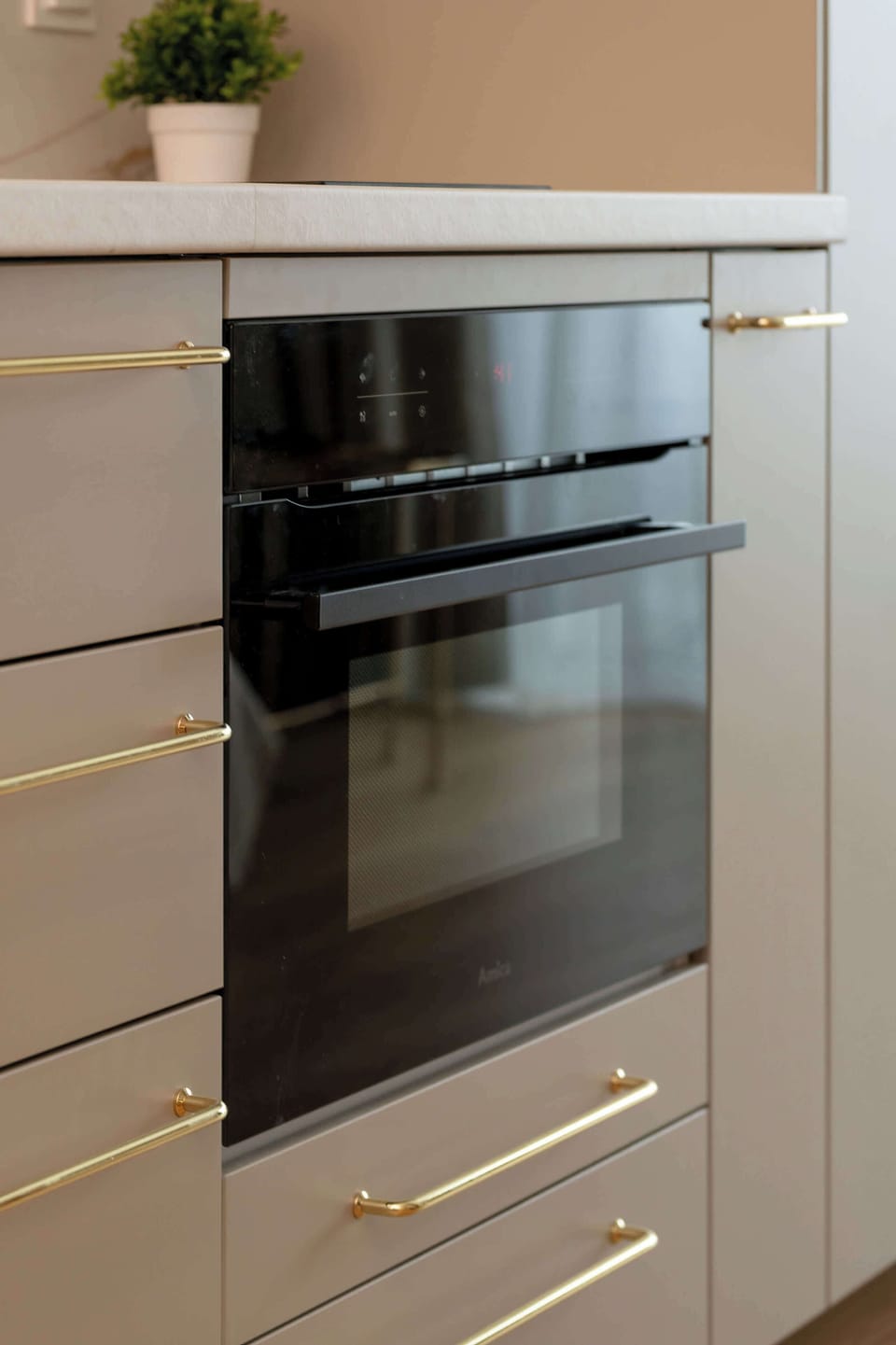A close-up view highlights a sleek, black-glass built-in oven integrated into light grey cabinetry. The vertical orientation of the shot emphasizes the high-end finishes and modern appliance design.