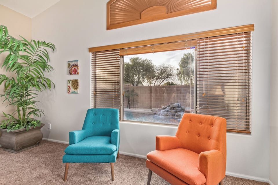 Unwind in your stylish seating nook with vibrant chairs and a stunning pool view through elegant blinds.