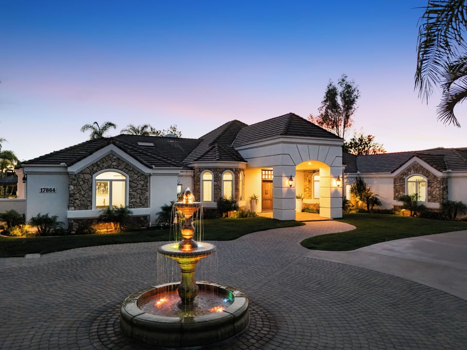 Grand Mediterranean‑style entrance with a circular drive, tiered fountain, and manicured palms.