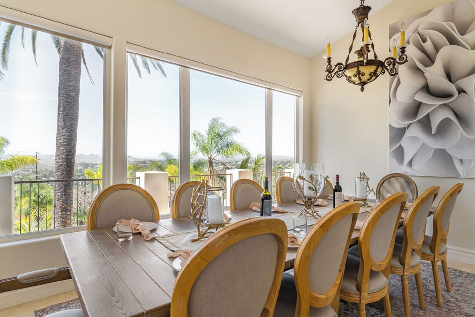 Bright dining space with a set table, warm wood tones, and expansive views framed by tall windows.