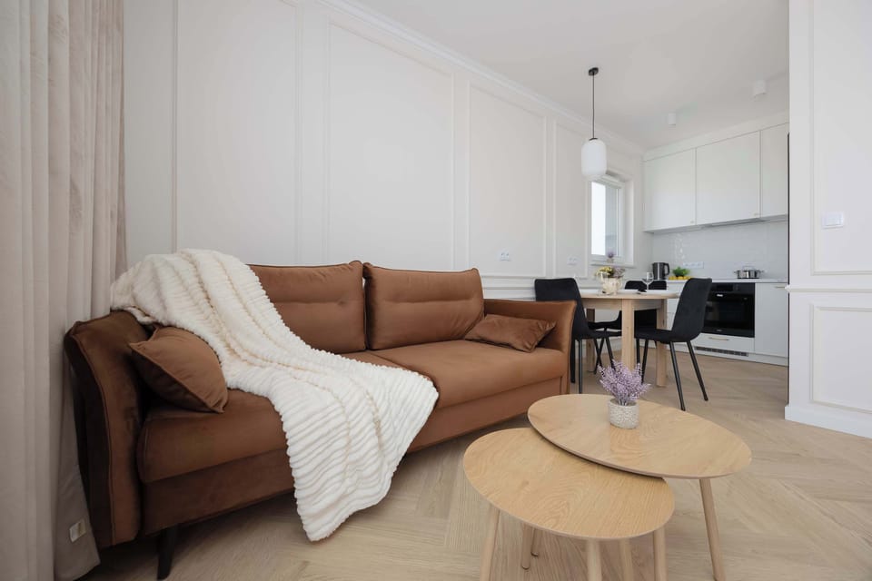 A cozy seating corner with a brown sofa covered by a light throw and a wooden coffee table. The open-plan layout connects seamlessly to the dining area in the background.