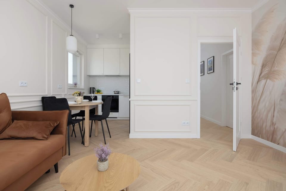 A bright and airy living space with a sofa, TV, and access to another part of the apartment. Clean lines and light colors emphasize a modern design.