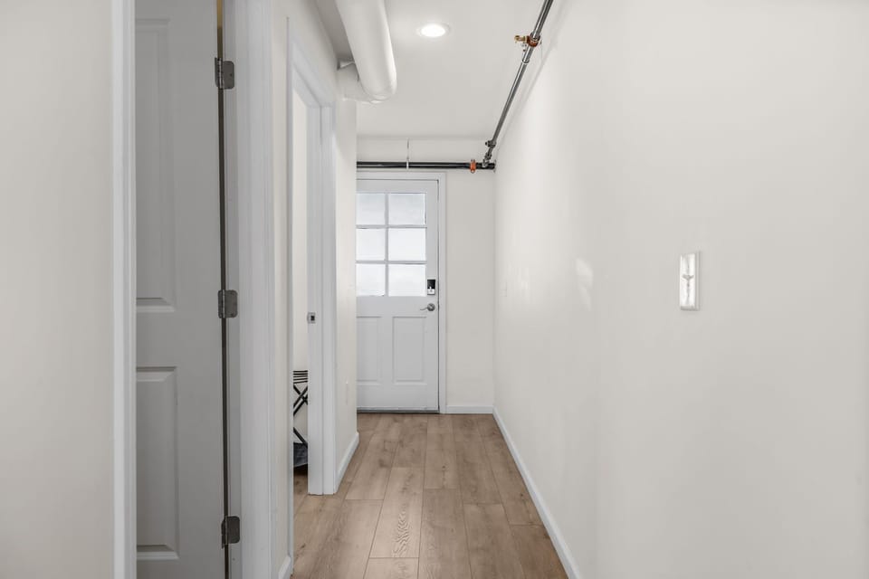 Interior hallway with white walls, wood-look flooring, and a white entry door.