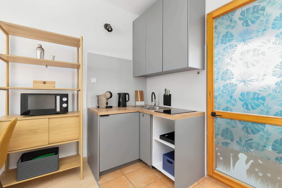 Another view of the kitchenette showing the fridge, microwave, and electric kettle. Wooden and gray finishes create a modern and functional studio environment.