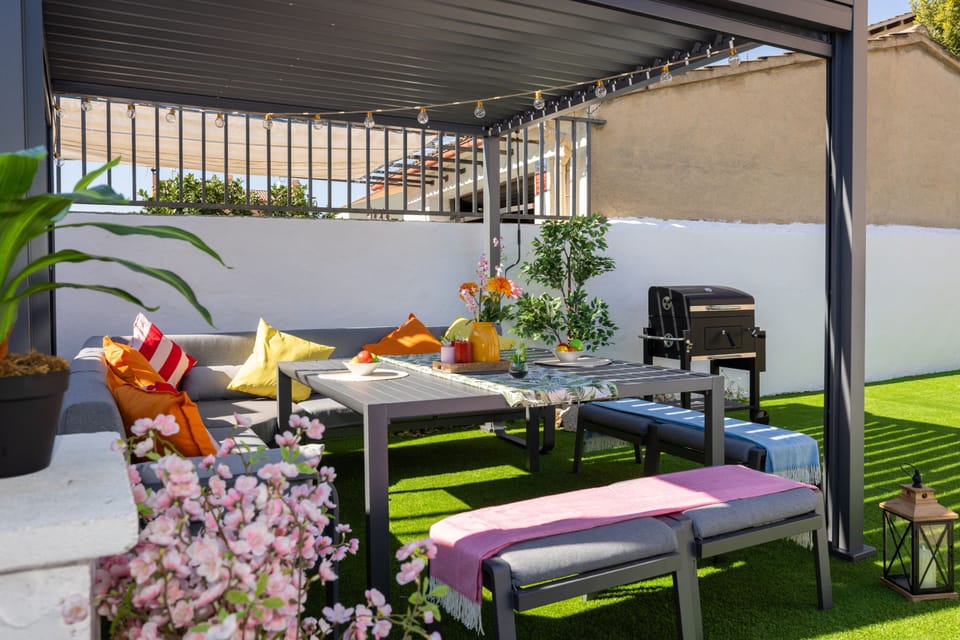 Covered patio with cozy seating, vibrant decor, and a BBQ grill for outdoor dining.