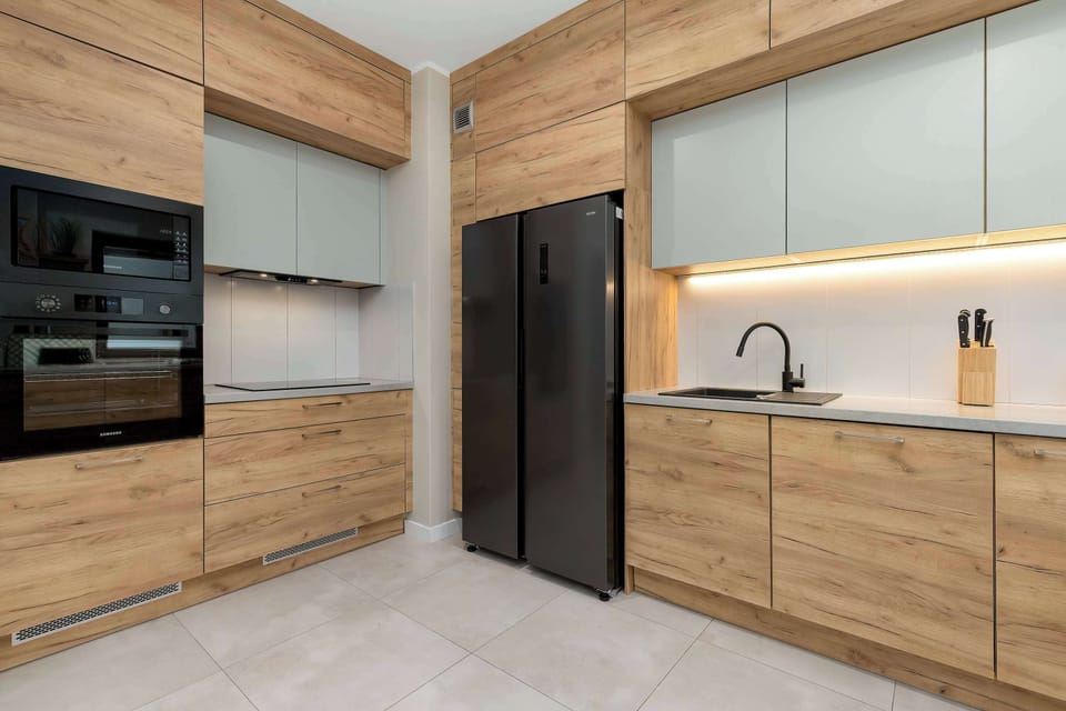 This view of the kitchen highlights the built-in oven and the clean lines of the wooden upper and lower cabinetry. The dark backsplash provides a modern contrast to the light wood tones.