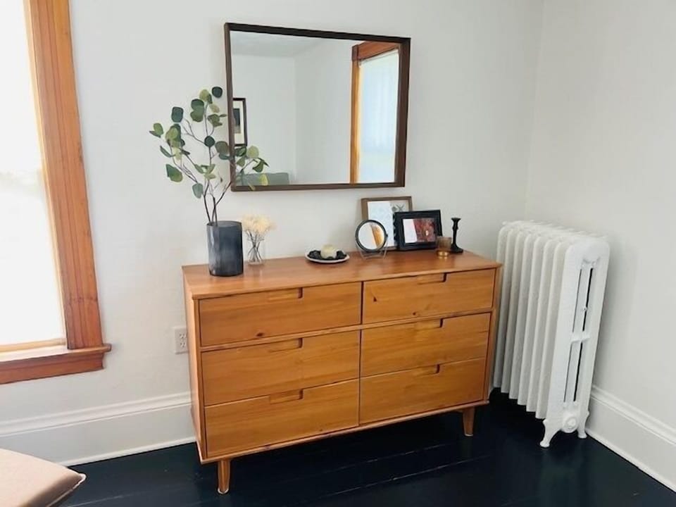 Your stylish bedroom dresser offers ample storage with warm wood tones, while natural light brightens the cozy space.