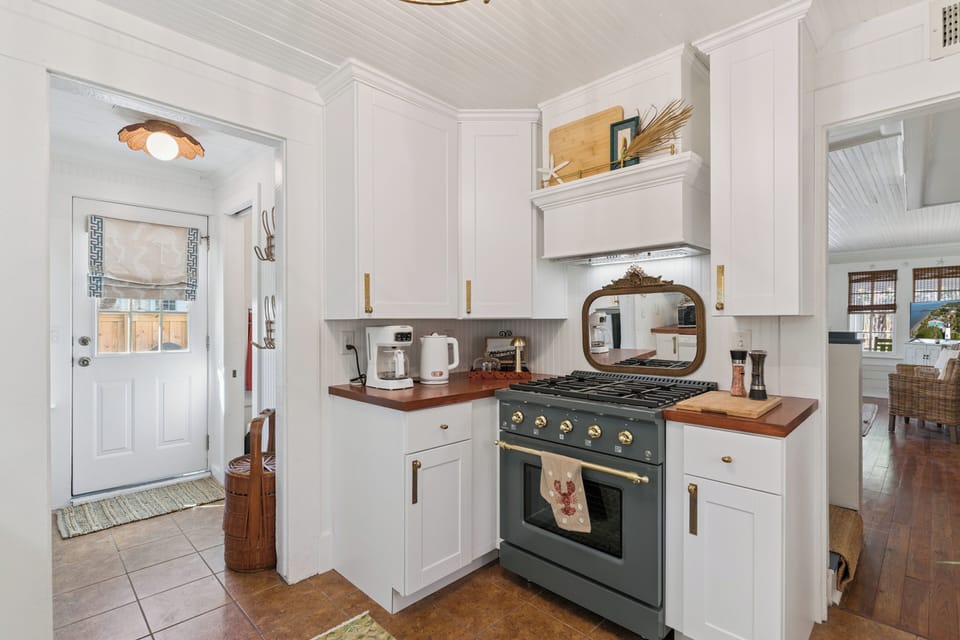 Step into your charming coastal kitchen, where white shaker cabinets meet warm wood counters and professional appliances await your culinary adventures.