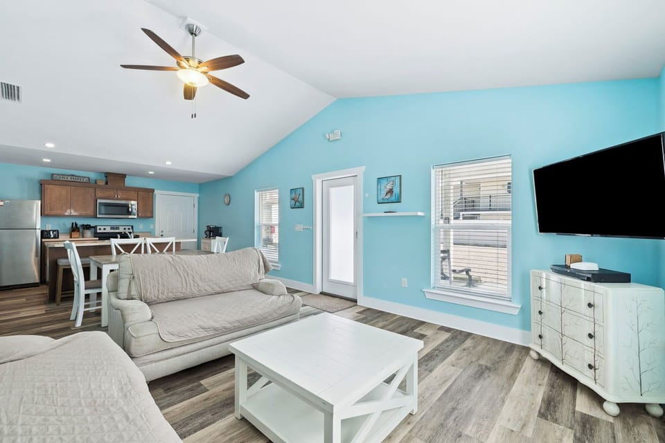 Relax in your bright, coastal-inspired living space with soft blue walls, comfortable seating, and modern amenities for your perfect getaway.
