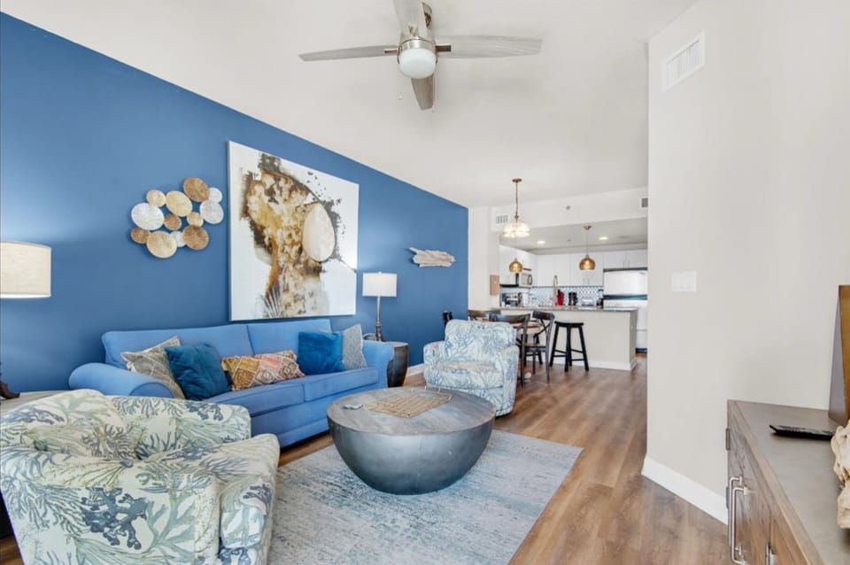 Unwind in your bright, coastal-inspired living space with ocean-blue accents, comfortable seating, and modern kitchen perfect for vacation relaxation.