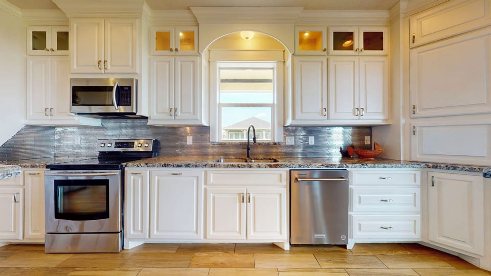 Gourmet kitchen with stainless steel appliances, granite countertops, custom white cabinetry, and farmhouse style layout.