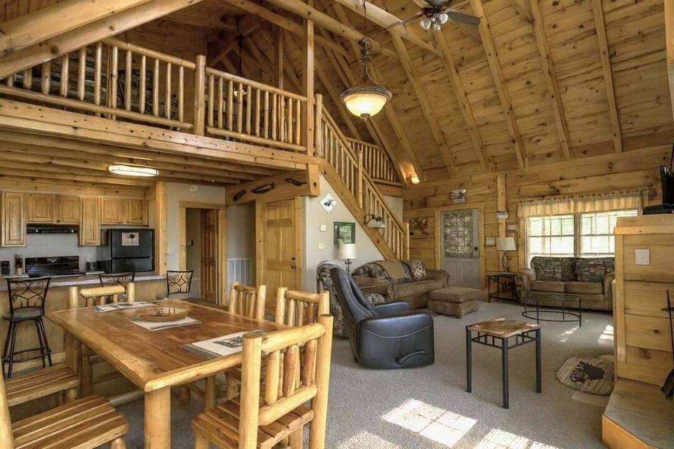 Open concept main level with living area, log dining table, and upper loft visible above at Mountain Paradise cabin in Wears Valley, Tennessee near Pigeon Forge