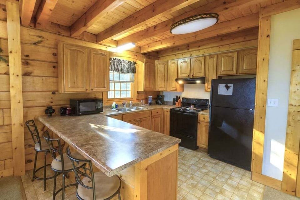 Fully equipped kitchen with island, three bar stools, black refrigerator, and all appliances at Mountain Paradise log cabin in Wears Valley, Tennessee